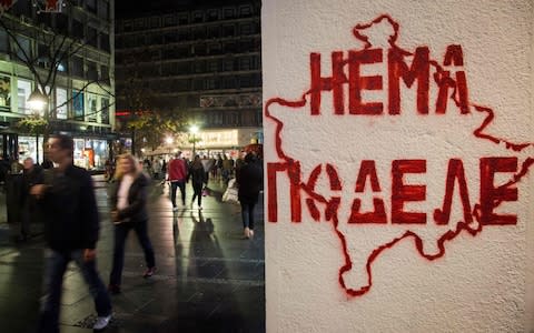 Pedestrians in Belgrade walk past a stencil depicting the map of Kosovo with the Cyrillic writing "No division" - Credit: VLADIMIR ZIVOJINOVIC/AFP/Getty Images