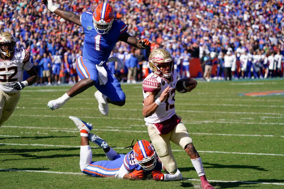 Florida State quarterback Jordan Travis (13) scrambles for a 9-yard touchdown run past Florida linebacker Brenton Cox Jr. (1) and linebacker Ty'Ron Hopper (28) during the first half of an NCAA college football game, Saturday, Nov. 27, 2021, in Gainesville, Fla. (AP Photo/John Raoux)