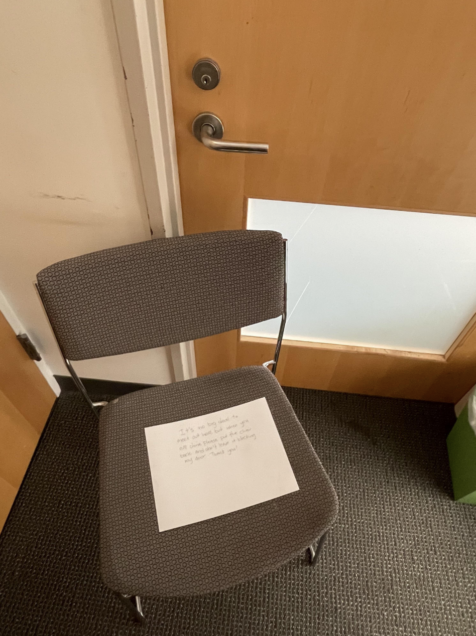 A chair sitting so close to a door that it's not possible to open the door; the chair has a note on it