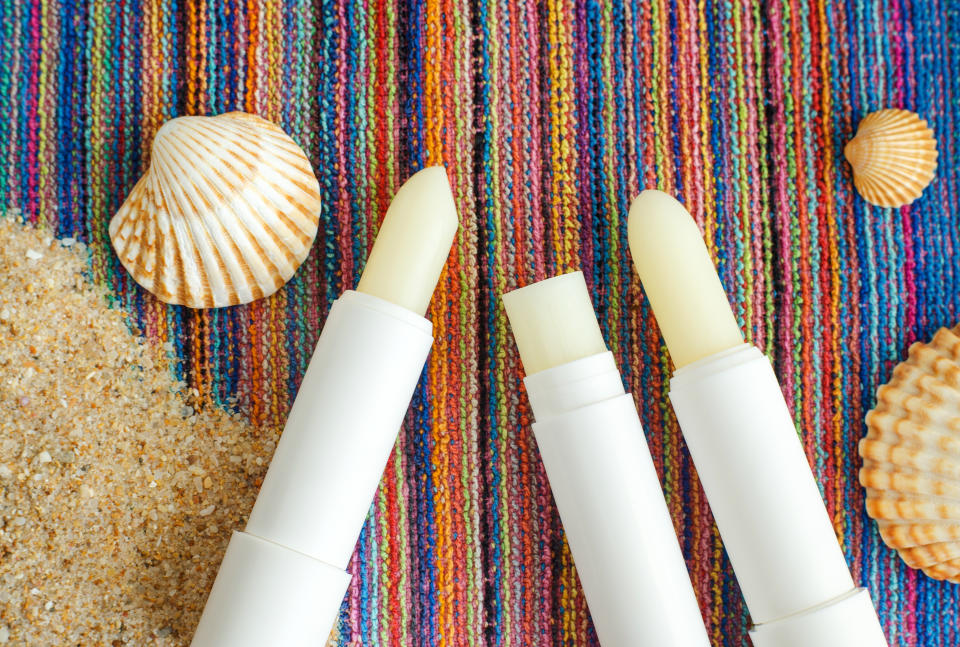 Three lip balms, sunscreen sticks on the colorful beach towel with sand and seashells. Dr. Pirani said he always recommends to patients they wear SPF, that includes lip balm. (Getty Images)