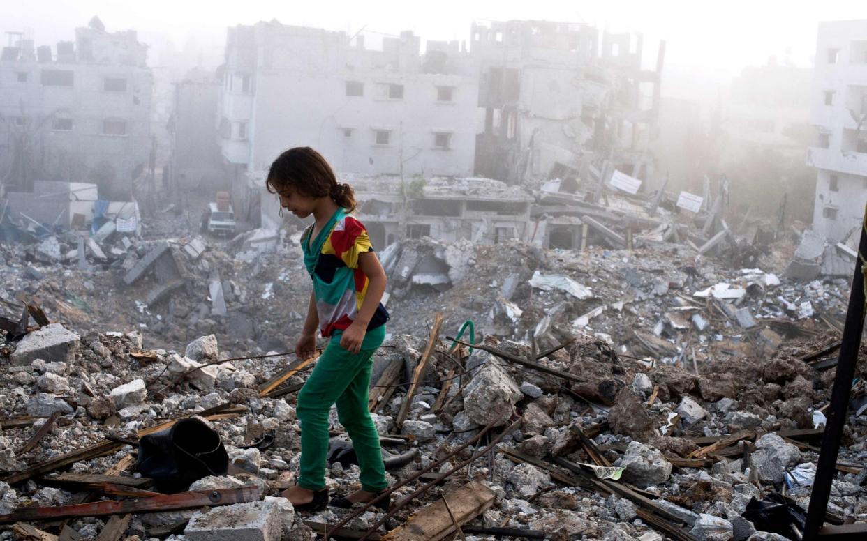 A Palestinian girl walks on the rubble-strewn ceiling of her family's home in Gaza City in 2014 - ROBERTO SCHMIDT /AFP