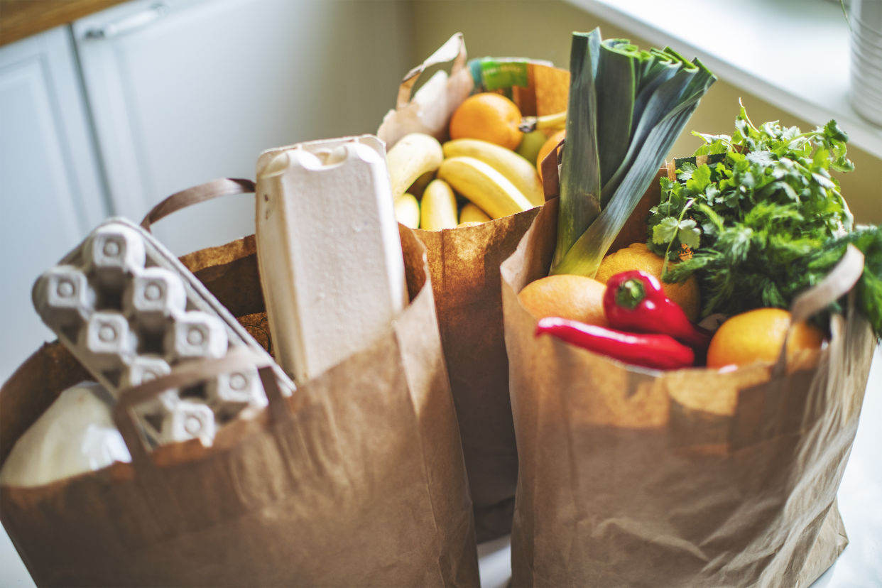 Focus on three brown paper bags filled with healthy groceries on an island in a kitchen with countertops in the background