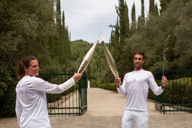 The first torch runner, 2020 Olympic rowing champion Stefanos Ntouskos (R), lights the torch, held by French Olympic silver medalist swimmer Laure Manaudou, at the start of her run with the Olympic flame after the lighting ceremony for the 2024 Olympic Games at the archaeological site of Ancient Olympia. Socrates Baltagiannis/