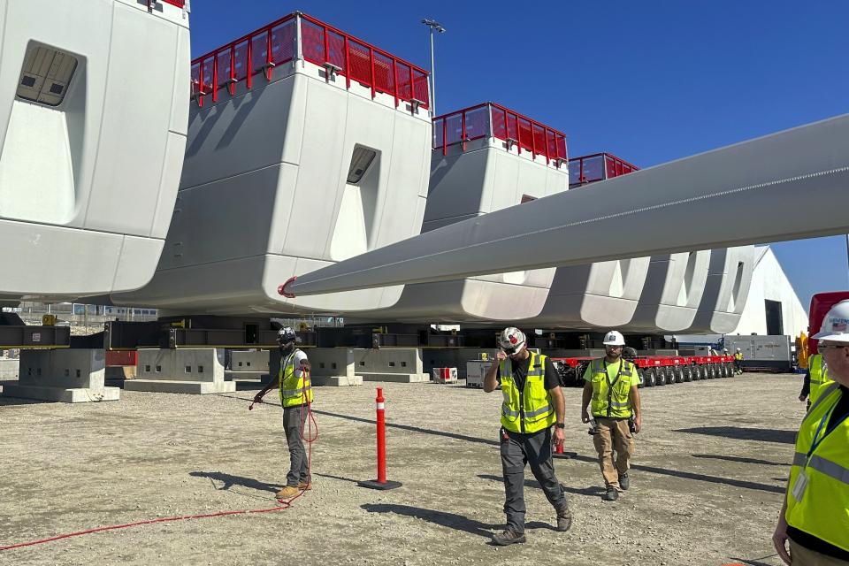 FILE - Workers walk by components of wind turbines being assembled at the State Pier in New London, Conn., Oct. 4, 2023. The turbines will make up South Fork Wind Farm and eventually provide energy to New York. (AP Photo/Susan Haigh, File)