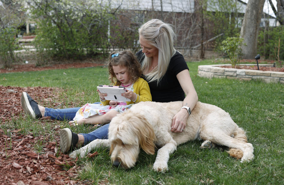 Katie Evers helps her 4-year-old daughter, Everlee, read a tablet while their goldendoodle lies next to them outside their home in southeast Denver on Thursday, April 30, 2020. Evers' partner, Eli Oderberg, like 30 million people around the United States who have filed for unemployment benefits after losing their jobs during the coronavirus pandemic, is facing the specter of paying the monthly rent with the flip of the calendar. (AP Photo/David Zalubowski)