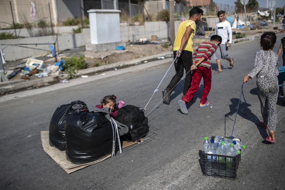 A child sits between plastic bags as migrants pull their belongings in Kara Tepe, near Mytilene the capital of the northeastern island of Lesbos, Greece, Thursday, Sept. 17, 2020. Greek police are moving hundreds of migrants to an army-built camp on the island of Lesbos Thursday after a fire destroyed an overcrowded facility, leaving them homeless for days. (AP Photo/Petros Giannakouris)