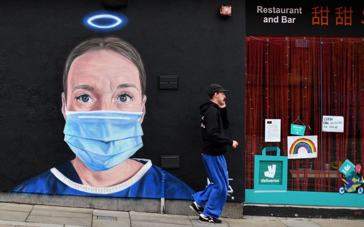 A pedestrian walks past street art depicting a nurse in scrubs and a face mask in Manchester. GPs are angry that NHS England rules will force them to treat patients who refuse to wear face coverings - Paul Ellis/AFP