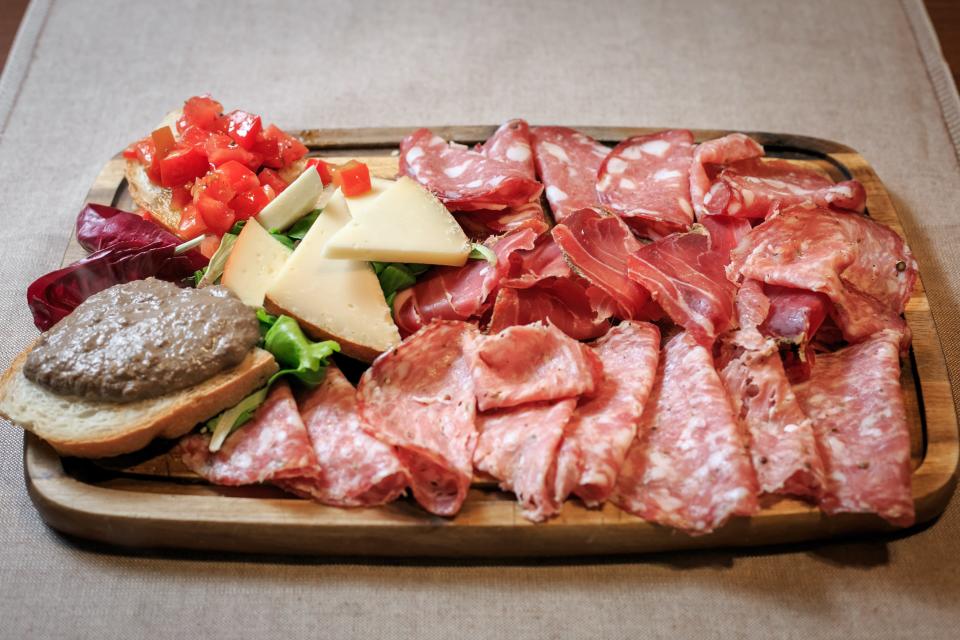 Charcuterie board on wooding board with folded salami and other meats and a few pieces of cheese