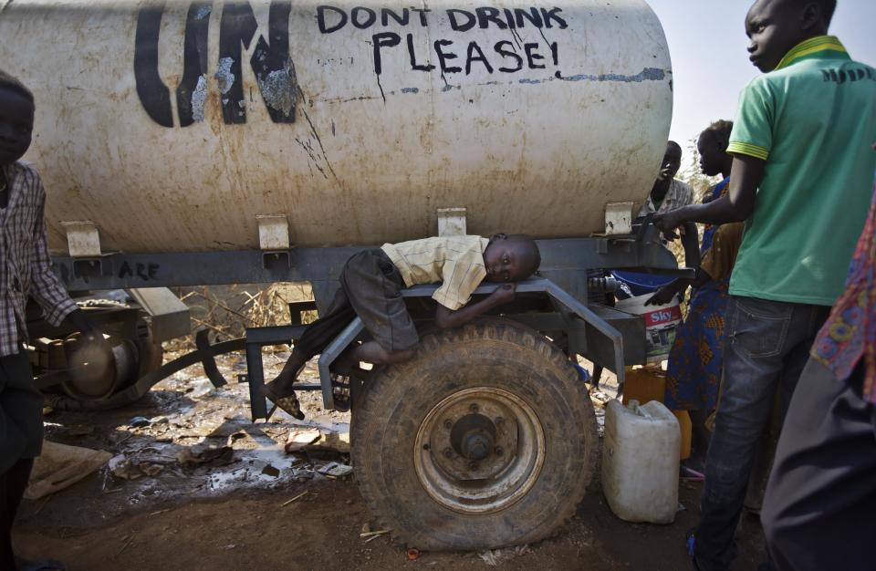 FILE - In this Tuesday, Dec. 31, 2013 file photo, a young displaced boy rests on the wheel arch of a water truck while others fill containers from it, at a United Nations compound which has become home to thousands of people displaced by the recent fighting, in the Jebel area on the outskirts of Juba, South Sudan. U.N. Secretary-General Ban Ki-moon on Wednesday, Jan. 15, 2014 strongly condemned the commandeering of humanitarian vehicles and the theft of food and other desperately needed aid by government and anti-government forces in violence-torn South Sudan. (AP Photo/Ben Curtis, File)