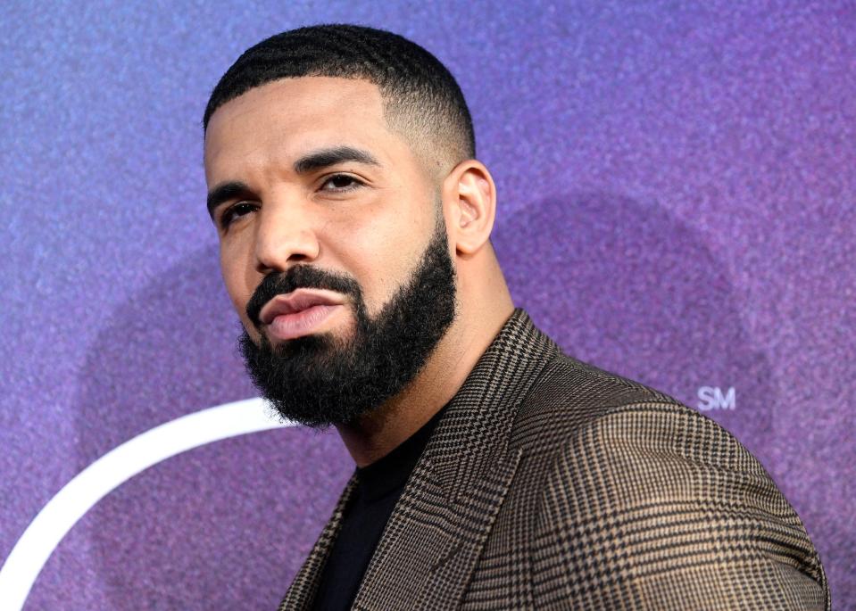 Drake in a suit from the shoulders up against a purple background.