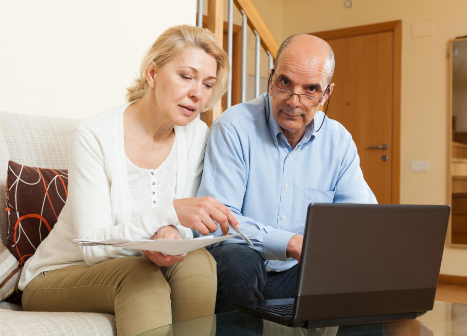 A mature couple examining their finances, with the husband visibly annoyed.