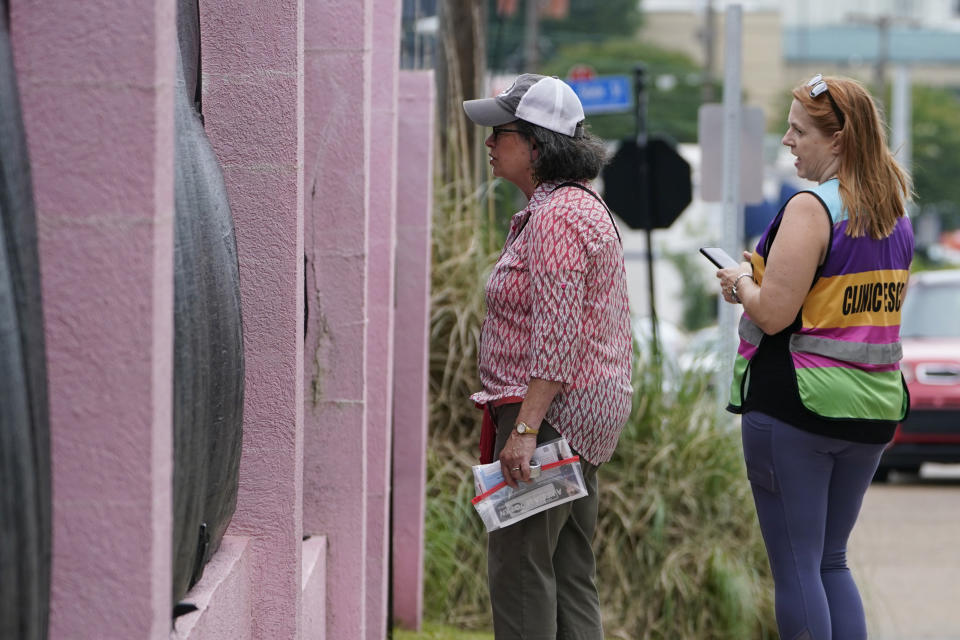 Pam Miller, an anti-abortion sidewalk counselor, left, speaks through the tarp draped fencing of the Jackson Womens Health Organization clinic, to an incoming patient at the front of the "pink house," while clinic escort Kim Gibson counters her statements, Thursday, May 20, 2021, in Jackson, Miss. The clinic is Mississippi's only state licensed abortion facility. On May 17, 2021, the U.S. Supreme Court agreed to take up the dispute over a Mississippi ban on abortions after 15 weeks of pregnancy. The issue is the first test of limits on abortion access to go before the conservative majority high court. Their decision could mean more restrictions, and focuses on the landmark 1973 ruling in Roe v. Wade, which established a woman's right to an abortion. (AP Photo/Rogelio V. Solis)