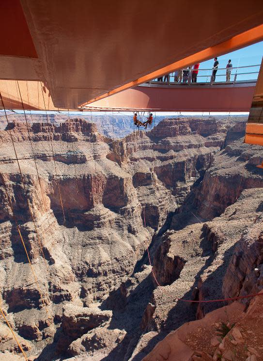 In this Tuesday, March, 25, 2014 photo provided by Abseilon USA via AZ Photos, technicians dangle from a series of ropes before polishing the underside glass at Grand Canyon Skywalk in Hualapai Reservation, Ariz. The more than 40 panes of glass underneath the horseshoe-shaped bridge on the Hualapai reservation aren’t easily accessible. The structure juts out 70 feet from the edge of the Grand Canyon, offering visitors a view of the Colorado River 4,000 feet below. (AP Photos/Abseilon USA, AZ Photos, George Walsh)