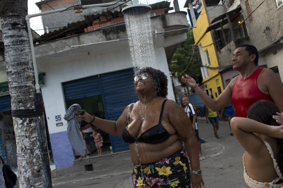A woman cools off in a street shower during the "Se Benze que da" block party, created by slain councilwoman Marielle Franco, in the Mare slum of Rio de Janeiro, Brazil, Saturday, Feb. 23, 2019. Merrymakers take to the streets in hundreds of open-air "bloco" parties ahead of Rio's over-the-top Carnival, the highlight of the year for many. (AP Photo/Silvia Izquierdo)
