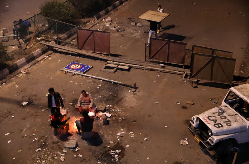 Local residents sit around a bonfire to keep themselves warm as they block a road during a protest against a new citizenship law, in New Delhi