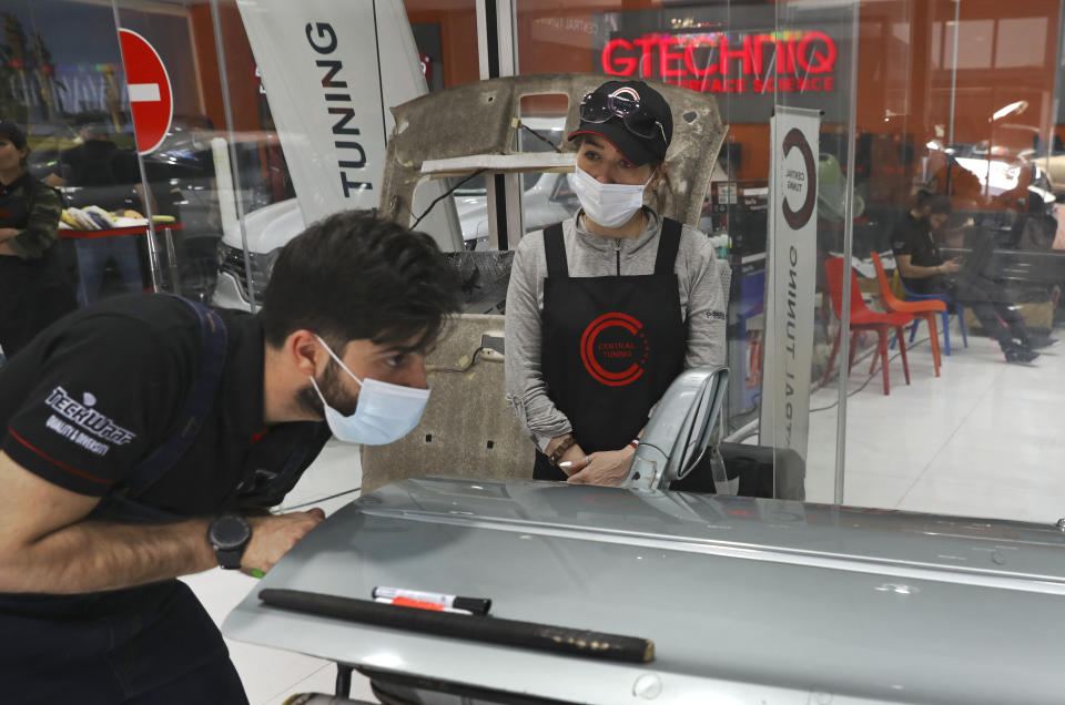 Female trainee Farahnaz Deravi watches a man repair a car door at a detailing shop in Tehran, Iran, Sunday, April 18, 2021. The auto industry remains male-dominated around the world, let alone in the tradition-bound Islamic Republic. Still Iranian women, especially in the cities, have made inroads over the years. (AP Photo/Vahid Salemi)