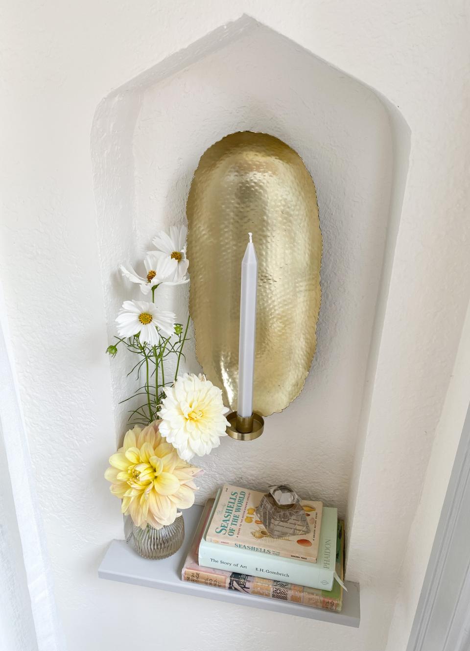 Seasonal blooms in a modern vase are displayed with favorite old books, a vintage inkwell and a new candle sconce.