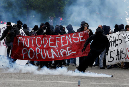 Tear gas floats in the air as demonstrators walk behind a banner which reads, "Populist Self-Defence" during clashes at the traditional May Day labour union march in Paris, France, May 1, 2017. REUTERS/Gonzalo Fuentes