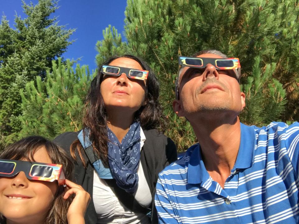 father, mother and daughter, family viewing solar eclipse with special glasses in a park