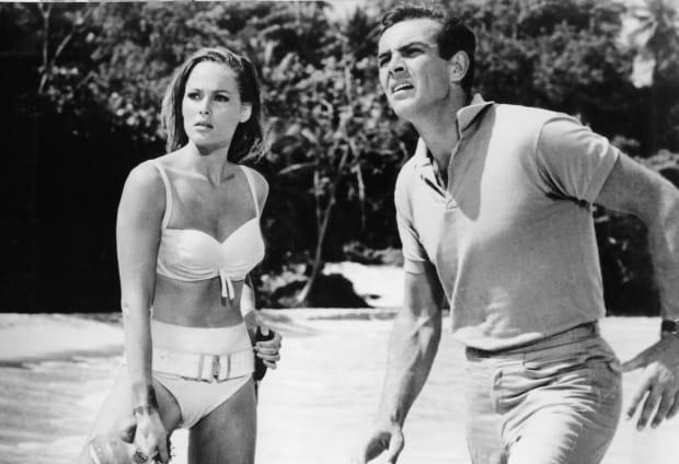 Sean Connery distracted at something he see's while standing near the water at a beach with Ursula Andress in a scene from the film 'James Bond: Dr. No', 1962.