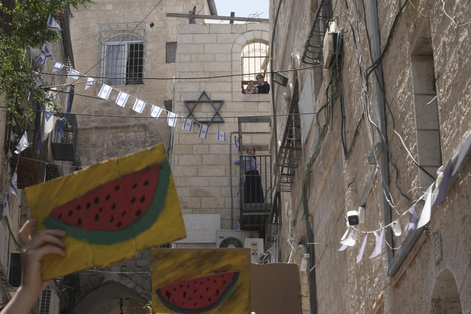 FILE - Jewish girls watch Israelis and Palestinians holding pictures of watermelon, a Palestinian symbol, as they protest the imminent eviction of a Palestinian family by a Jewish settler organization outside their home in the Muslim Quarter of the Old City of Jerusalem, June 16, 2023. Watermelons have emerged on banners, t-shirts, cars and social media over the past three months in protests against the Israel-Hamas war. From New York and Tel Aviv to Dubai and Belgrade, the fruit has caught on globally as a symbol of solidarity with the Palestinian people. (AP Photo/Mahmoud Illean, File)