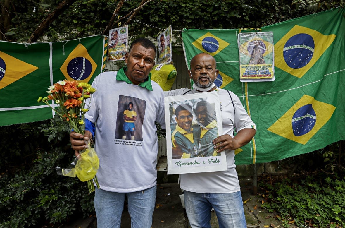 Antonio da Paz, left, and Renato Souza stand in front of the Albert Einstein Hospital holding memorabilia honoring Brazilian soccer star Pele, in Sao Paulo, Brazil, Friday, Dec. 30, 2022. Edson Arantes do Nascimento, known to the world as Pele, died at the hospital Thursday at the age of 82. (AP Photo/Marcelo Chello)