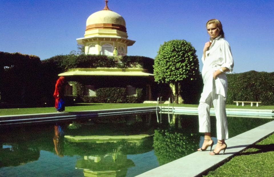 Model, Patti Hansen wearing Emanuel Ungaro narrow silk ankle-pants and thin shirt-tunic in cream and coffee stripes, standing poolside at India’s Rajmahal Palace Hotel.