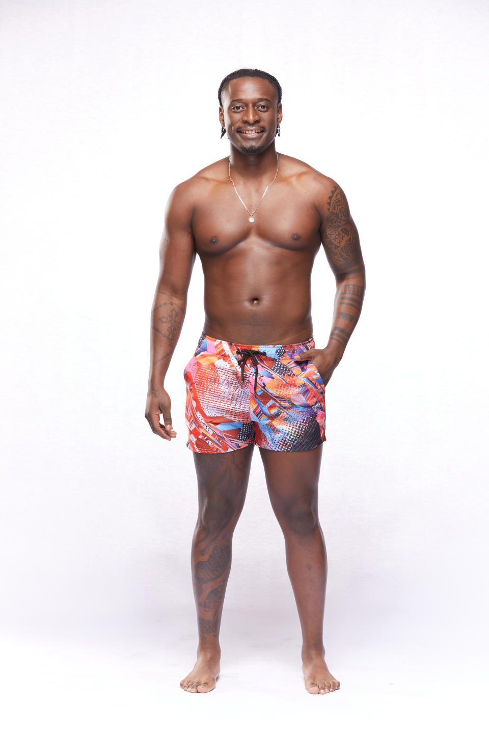 Contestant Tak stands smiling in board shorts against a white background