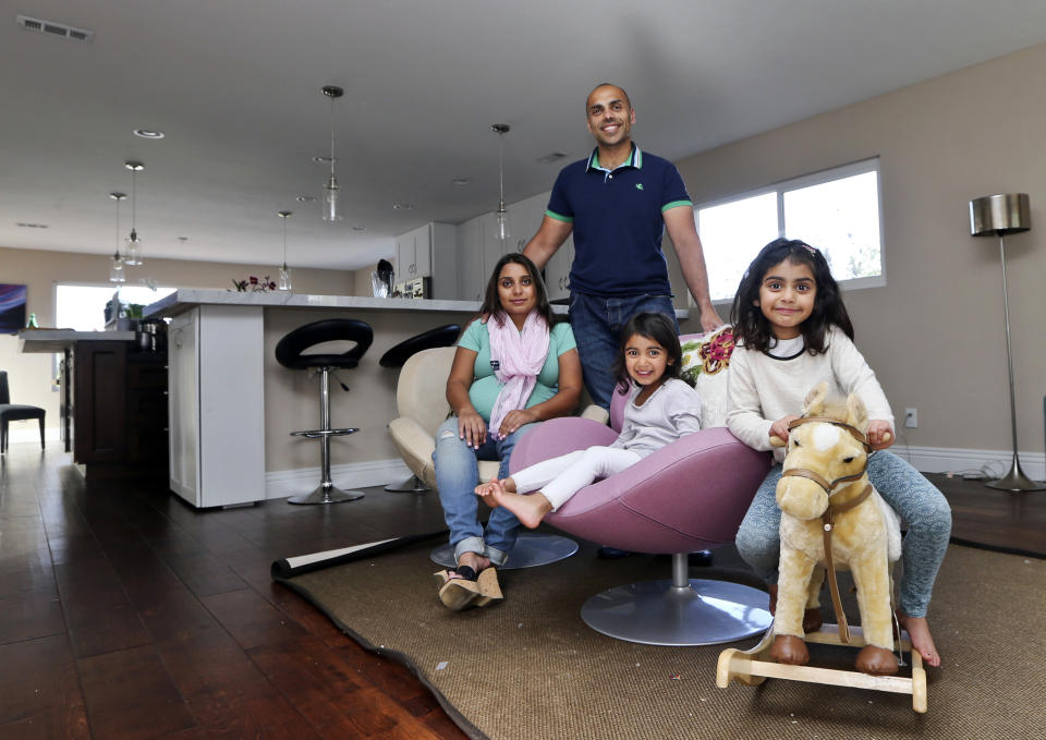 In this April 16, 2014 photo, the Jaswal family, Imran, standing, his wife Aniqa, left, and daughters, Arissa, right, and Jayda, pose for photos in the family room at their home in La Jolla, Calif. The couple bought the four-bedroom house about 10 minutes from the beach in Febrauary. Once Imran’s management consulting business began flourishing, the couple felt comfortable enough after years of renting to buy their first home. (AP Photo/Lenny Ignelzi)