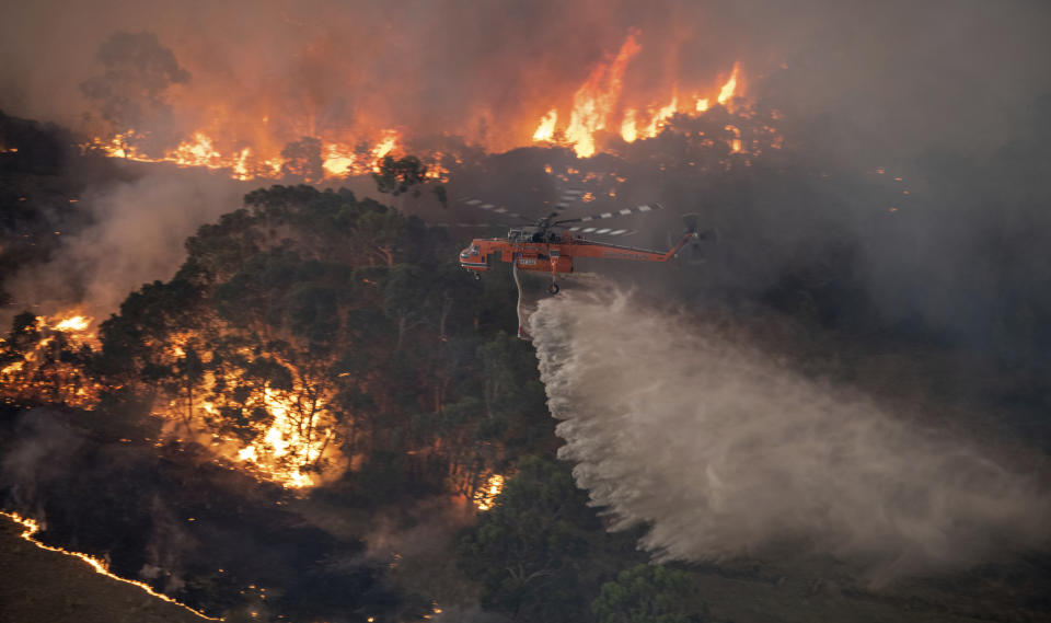 In this Monday, Dec. 30, 2019 photo provided by State Government of Victoria, a helicopter tackles a wildfire in East Gippsland, Victoria state, Australia. Wildfires burning across Australia's two most-populous states trapped residents of a seaside town in apocalyptic conditions Tuesday, Dec. 31, and were feared to have destroyed many properties and caused fatalities. (State Government of Victoria via AP)