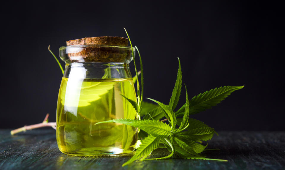 A jar containing a light greenish liquid next to a cannabis leaf.