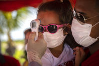 A little girl wearing a face mask amid the new coronavirus pandemic gets her temperature taken at a police checkpoint, at the entrance to the province of Havana, Cuba, Monday, Aug. 10, 2020. Cuban authorities on Monday re-imposed measures aimed at containing the spread of COVID-19, restricting inter-provincial travel, closing beaches, bars, restaurants, and keeping the main airport closed to international travel. (AP Photo/Ramon Espinosa)