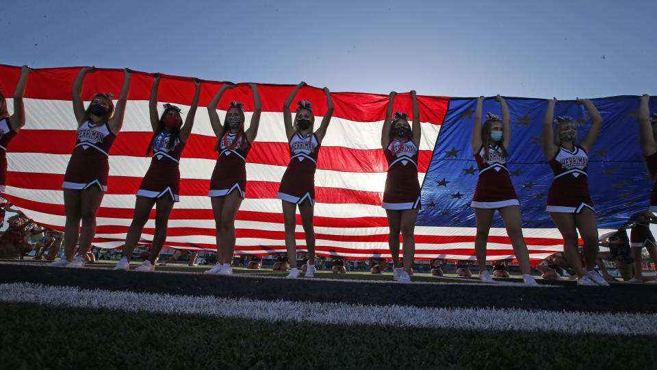 Herriman cheerleaders raise the American flag before the start of a high school football game between Davis and Herriman on Thursday, Aug. 13, 2020, in Herriman, Utah. Utah is among the states going forward with high school football this fall despite concerns about the ongoing COVID-19 pandemic that led other states and many college football conferences to postpone games in hopes of instead playing in the spring. (AP Photo/Rick Bowmer)