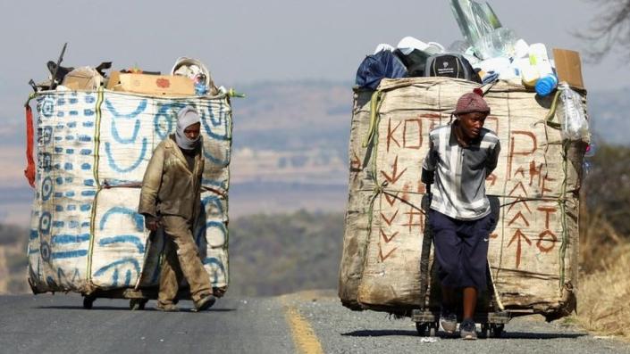 Steven Lesoona and Thabang Pule, waste pickers, pull trolleys loaded with recyclable materials, in Naturena, near Johannesburg