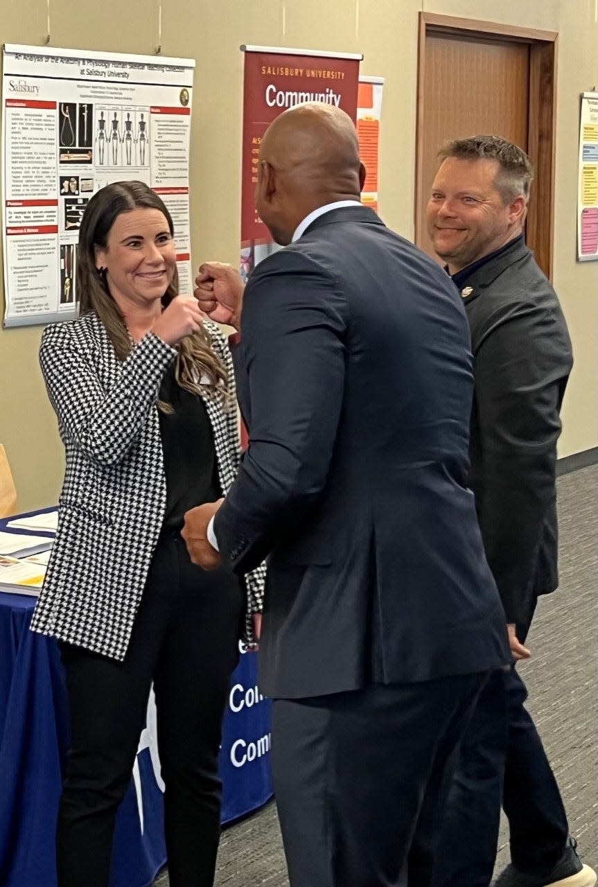 At left, Wicomico County Executive Julie Giordano, a Republican, bumps fists with Gov. Wes Moore, a Democrat, before Moore spoke at a Federal Communications Commission event held at Salisbury University on August 29, 2023. State Del. Carl Anderton Jr., R-Wicomico, smiles in the background.