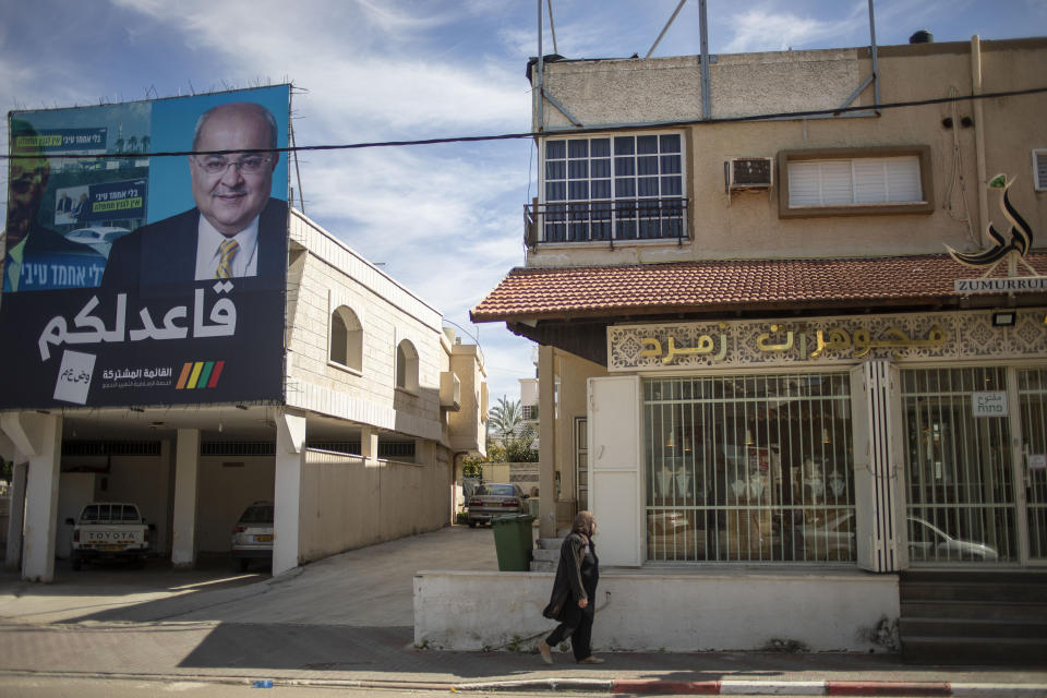 In this Thursday, March 5, 2020 photo, Israeli Arab woman walks past an election campaign poster showing Israeli Politician Ahmad Tibi of the Joint List in Tira, Israel. A surge in Arab voter turnout was key to depriving Prime Minister Benjamin Netanyahu and his nationalist allies of a parliamentary majority in this week’s Israeli election. Undercutting Netanyahu’s ambitions was celebrated as sweet payback in the nearly 2 million-strong minority that the hard-line leader had relentlessly tried to tarnish as disloyal to the state. The Arabic reads, "I sit with you." (AP Photo/Ariel Schalit)