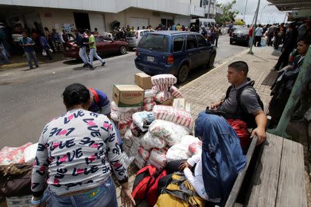 People sit next to bags filled with staple items while they wait for transportation in Pacaraima, Brazil August 3, 2016. REUTERS/William Urdaneta