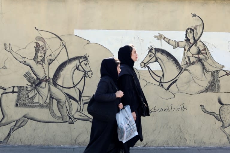 Dos mujeres con velo pasan por delante de un mural con una ilustración del poema épico persa "Shahnama" ("Libro de los reyes"), en el centro de Teherán, el 30 de enero de 2024 (Atta Kenare)