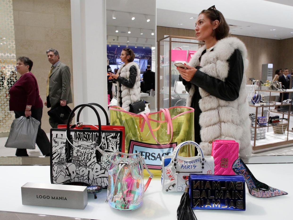 Woman holds phone while standing near display of handbags at Neiman Marcus store