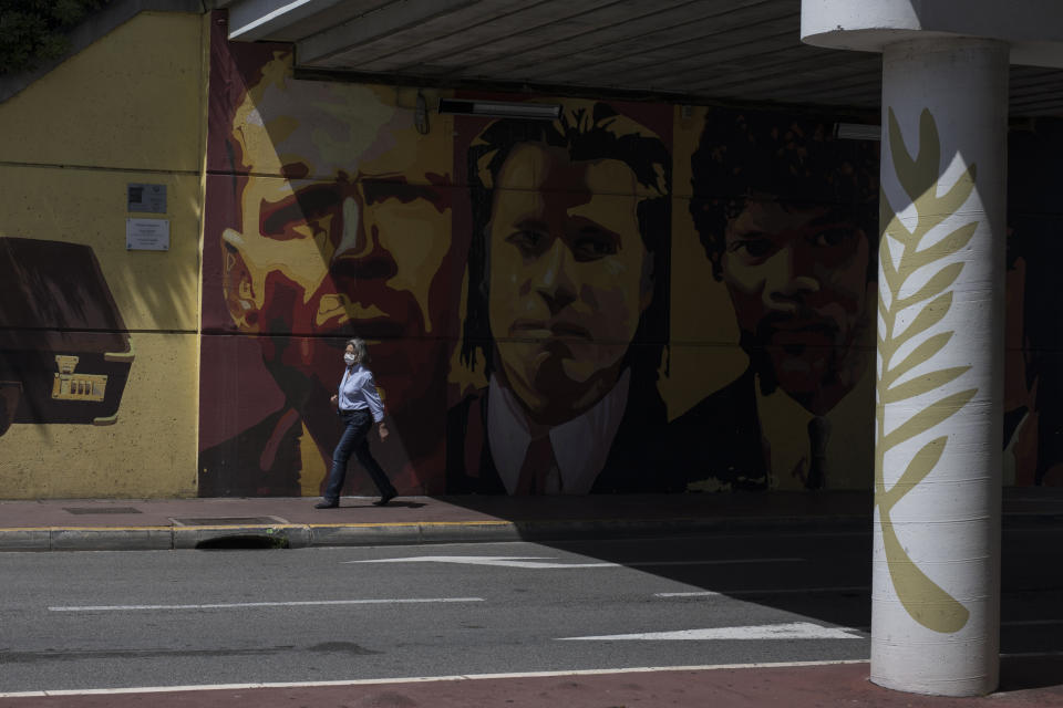 A woman wearing a face mask to protect against coronavirus walks by a mural depicting characters from the film Pulp Fiction in Cannes, southern France, Tuesday, May 12, 2020. The Cannes Film Festival won't kick off as planned on Tuesday. The festival's 73rd edition has been postponed indefinitely, part of the worldwide shutdowns meant to stop the spread of the coronavirus. (AP Photo/Daniel Cole)