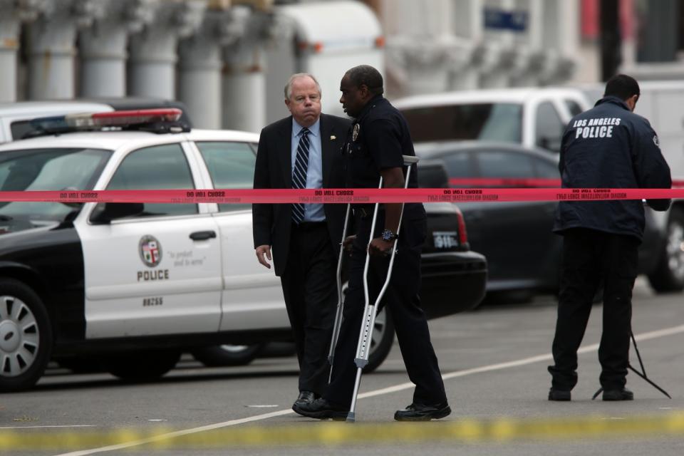 Clifford Proctor walks on crutches alongside an LAPD cruiser.