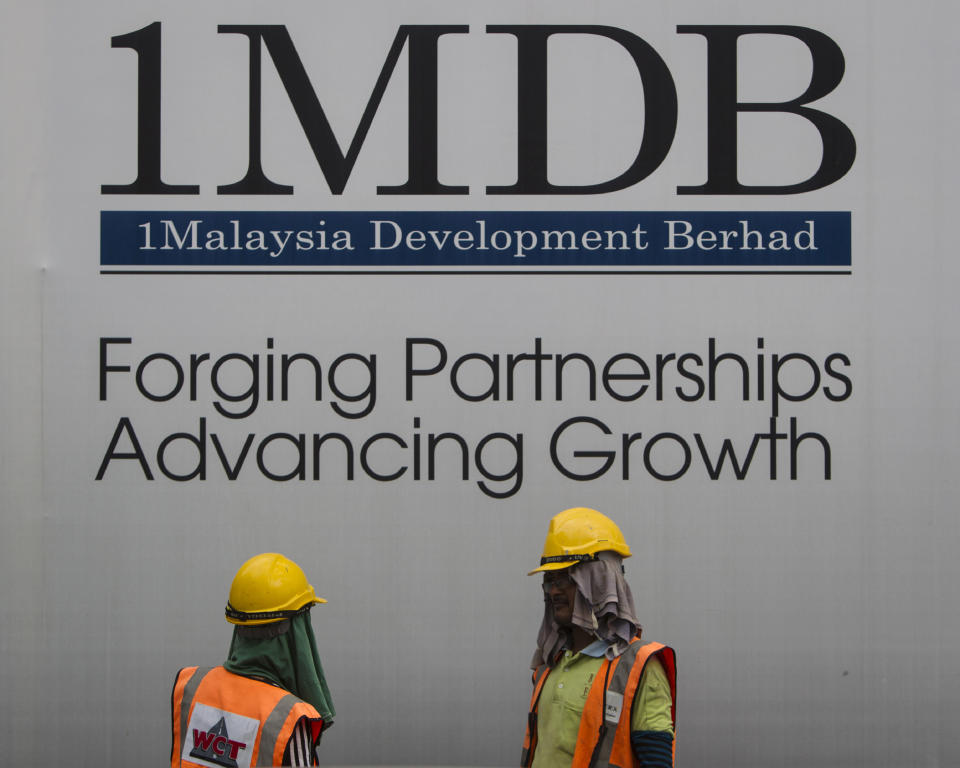 FILE - In this May 14, 2015 file photo, construction workers chat in front of a billboard for state investment fund 1 Malaysia Development Berhad (1MDB) at the fund's flagship Tun Razak Exchange development in Kuala Lumpur, Malaysia. A subsidiary of Goldman Sachs has pleaded guilty to federal charges in the U.S. and agreed to pay more than $2 billion in a foreign corruption probe tied to a Malaysian sovereign wealth fund that was looted of billions of dollars. The company, Goldman Sachs Malaysia, entered the plea in federal court in Brooklyn borough of New York on Thursday, Oct. 22, 2020. (AP Photo/Joshua Paul, File)