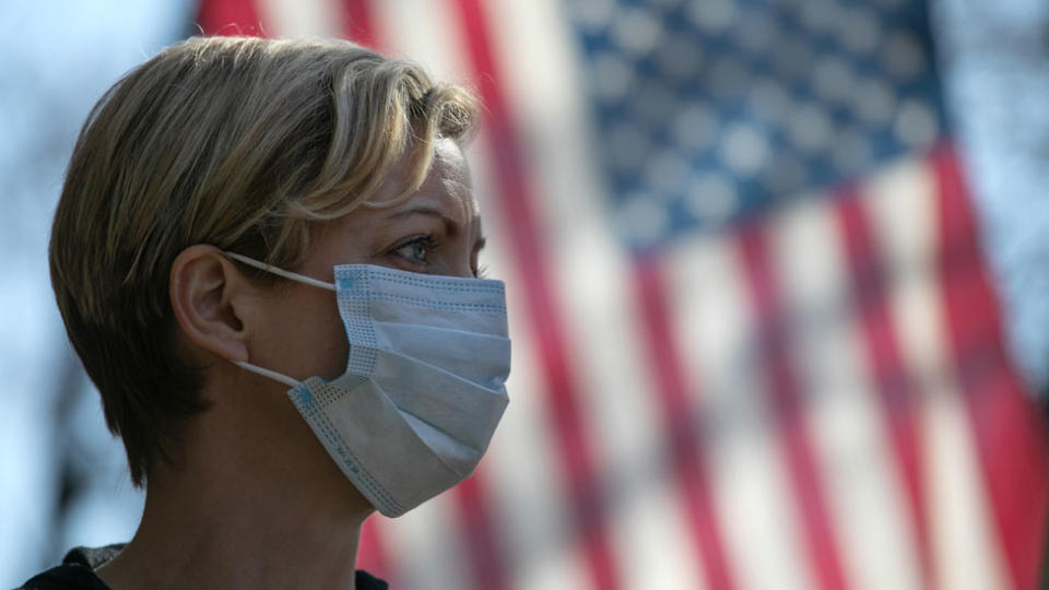 Una mujer usando una mascarilla junto a la bandera de Estados Unidos.