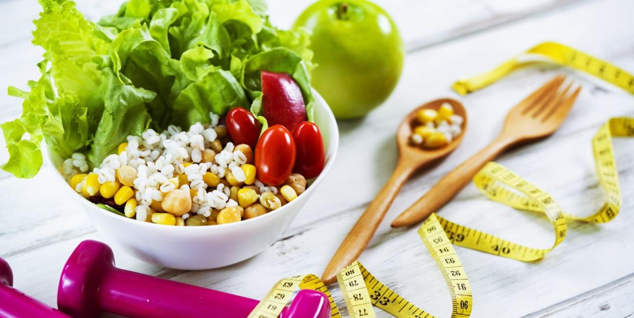 healthy eating and exercising with healthy salad and dumbbells and tape measure