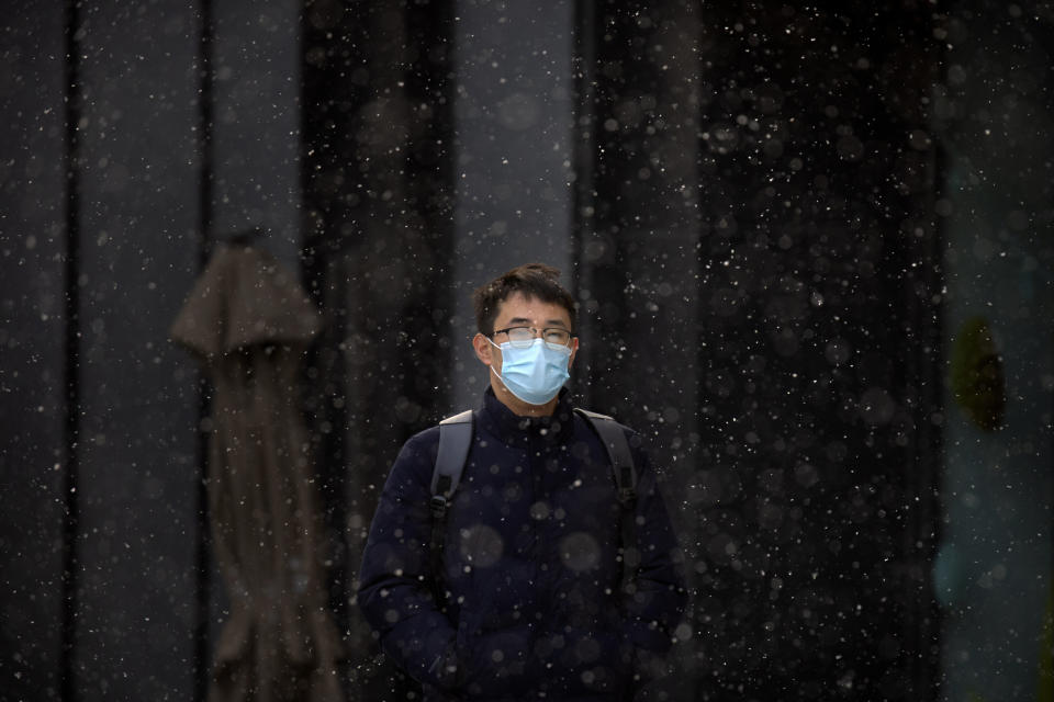 A man wearing a face mask to protect against the spread of the coronavirus walks along a street during a snowy morning in Beijing, Tuesday, Jan. 19, 2021. A Chinese province near Beijing grappling with a spike in coronavirus cases is reinstating tight restrictions on weddings, funerals and other family gatherings, threatening violators with criminal charges. (AP Photo/Mark Schiefelbein)