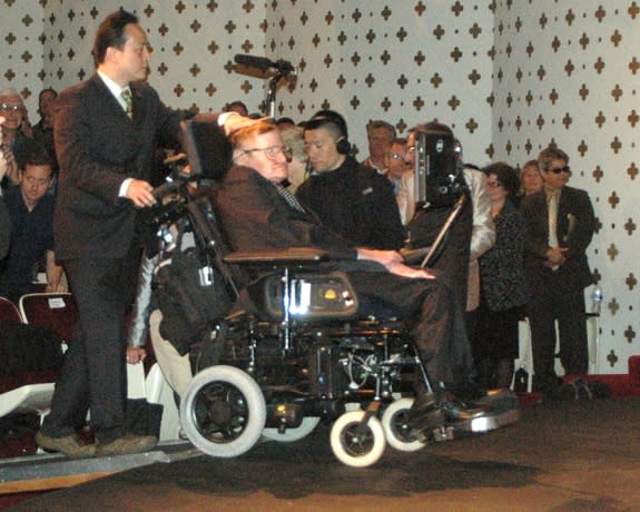 Dr. Stephen Hawking is brought onstage by a helper to give his presentation, "The Origin of the Universe," at Caltech on April 16, 2013.