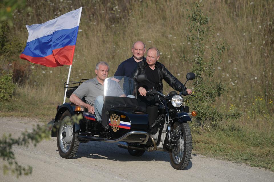 Russian President Vladimir Putin drives a motorbike during the Babylon's Shadow bike show camp near in Sevastopol, Crimea, Saturday, Aug. 10, 2019. Head of the Republic of Crimea Sergei Aksenov, is in sidecar, and acting Governor of Sevastopol Mikhail Razvozhaev, rides pillion. (Alexei Druzhinin, Sputnik, Kremlin Pool Photo via AP)