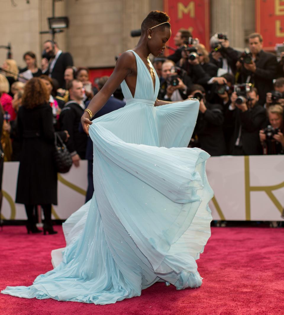 Lupita Nyong'o in a flowing dress with photographers in the background