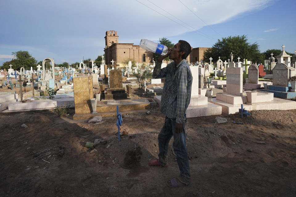 A Yaqui Indigenous homeless drinks water from a bottle that holding flowers decorating a tomb at the cemetery where slain water-defense leader Tomás Rojo is buried in Potam, Mexico, Tuesday, Sept. 27, 2022. With little water, widespread poverty and no farm work available, younger Yaquis have begun to migrate to nearby cities and the U.S. border city of Nogales and seldom return, threatening the survival of Yaqui culture. (AP Photo/Fernando Llano)