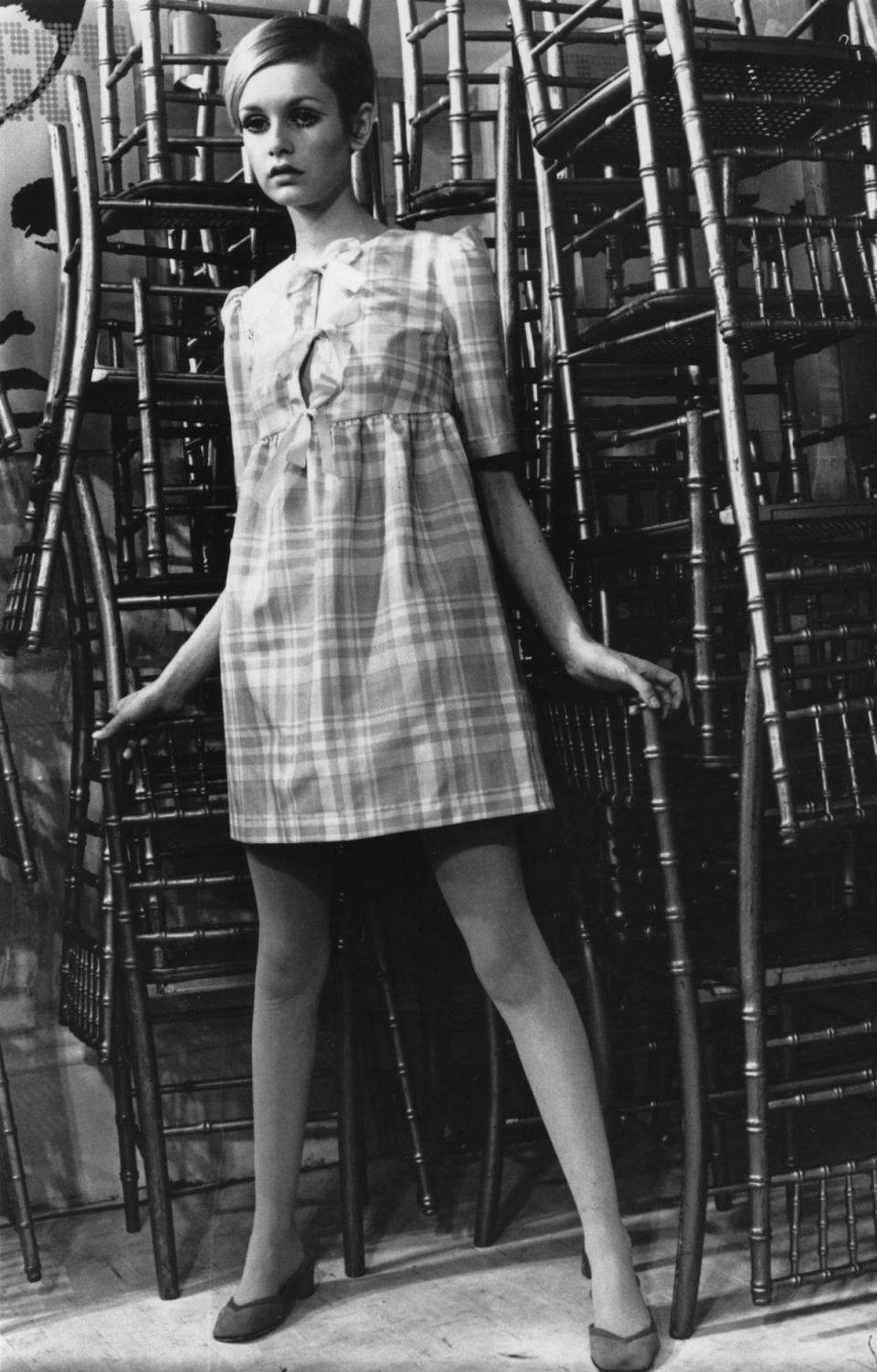 Twiggy, originally Lesley Hornby, poses in font of a stack of chairs. (Getty Images)
